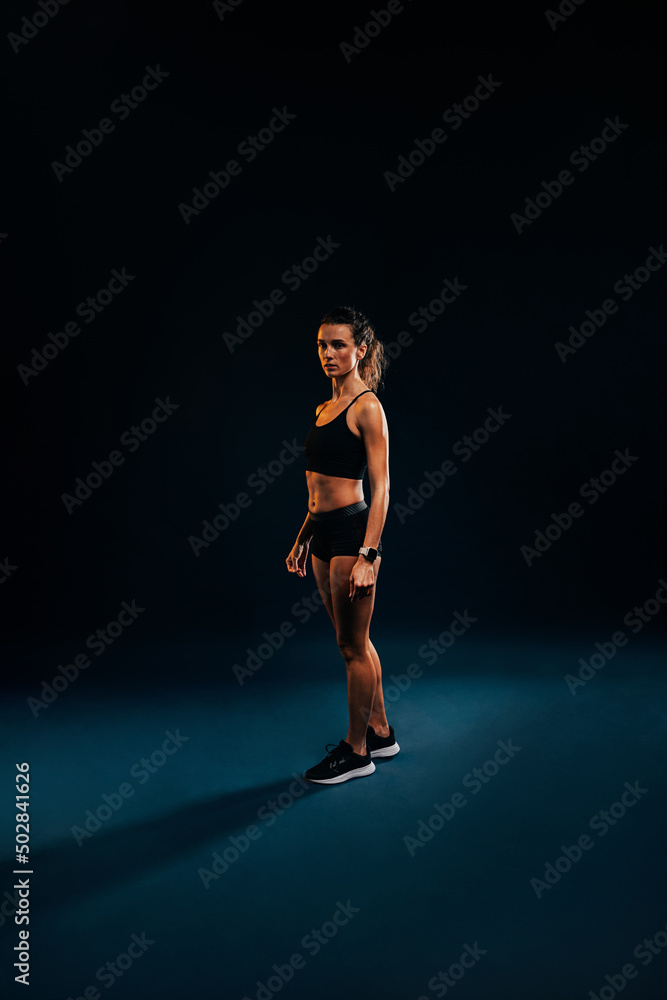 Portrait of young woman in sportswear relaxing on black background during training