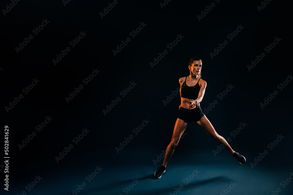 Healthy strong woman jumping from side to side on black background warming up