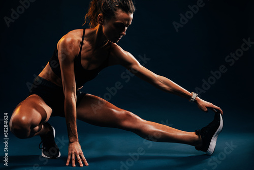 Athlete doing stretching exercises on black background. Female runner stretching leg muscles by touching his shoes while sitting in studio.