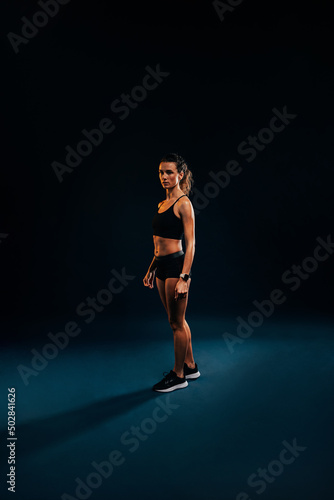 Portrait of young woman in sportswear relaxing on black background during training