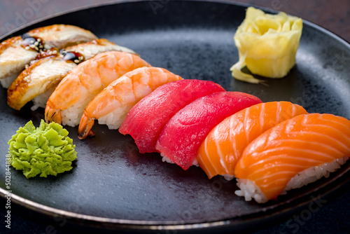 sushi salmon,sushi tuna,sushi with shrimp, sushi with eel on a black plate on blue concrete table macro close up