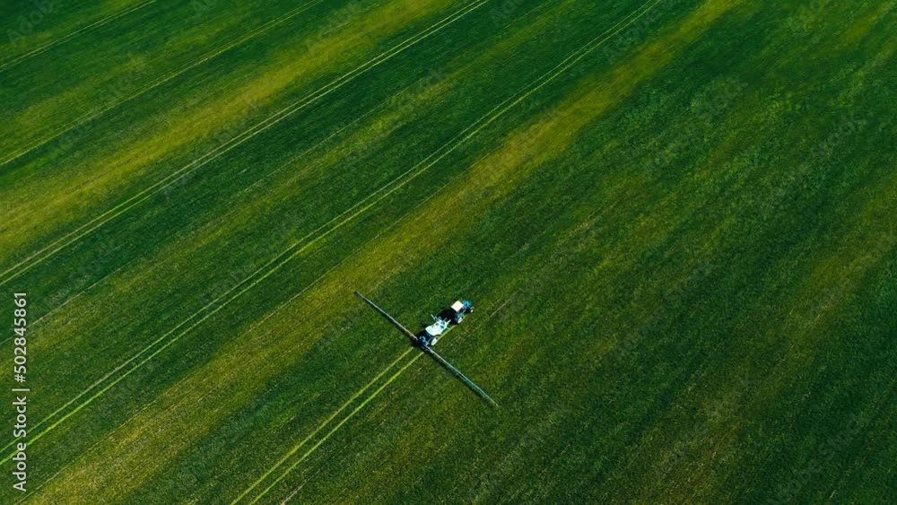 Aerial view of a tractor operating in green fields. The tractor sprays water or fertilizer on wheat, cereals, rye or corn flakes. The process is part of agriculture and growing food for mass consumpti Aerial view of a tractor operating in green fields. The tractor sprays water or fertilizer on wheat, cereals, rye or corn flakes. The process is part of agriculture and growing food for mass consumpti
