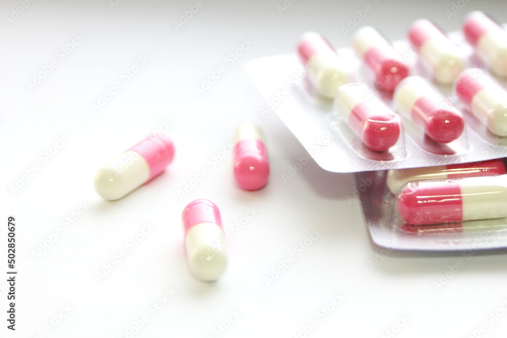 Pink-green pill capsules were placed on a white table. Pink-green pill capsules were placed on a white table.