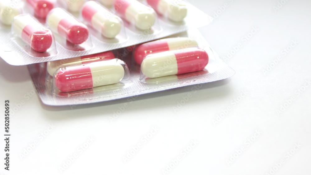Pink-green pill capsules were placed on a white table. Pink-green pill capsules were placed on a white table.