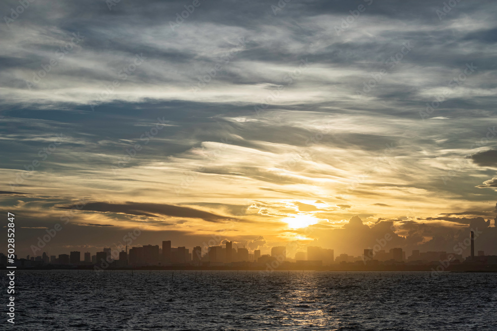 舞浜から見た東京湾岸のビルの合間に落ちる夕陽