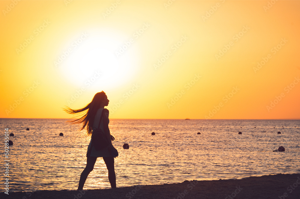 lone woman walking along sea beach at sunset
