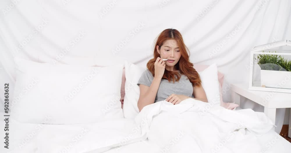 Asian woman in blanket measuring temperature by thermometer at home. Healthcare concept Asian woman in blanket measuring temperature by thermometer at home. Healthcare concept