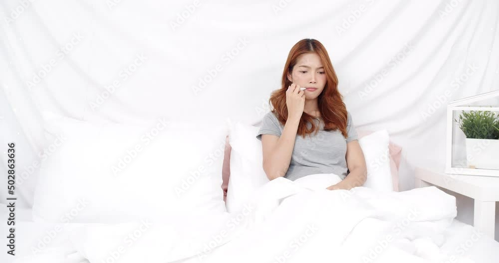 Caucasian Asian woman has a sick thermometer not feeling well and coughing while sitting in bed at home. Healthcare concept Caucasian Asian woman has a sick thermometer not feeling well and coughing while sitting in bed at home. Healthcare concept