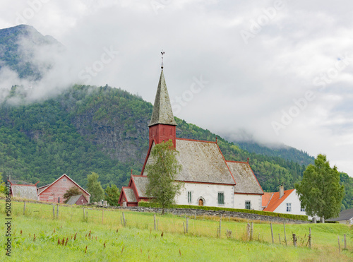 Medieval 12 century gothic stone Dale church in Luster village on Lustrafjord in Norway. White plastered stone walls, green grass and mountain slopes, cloudy sky