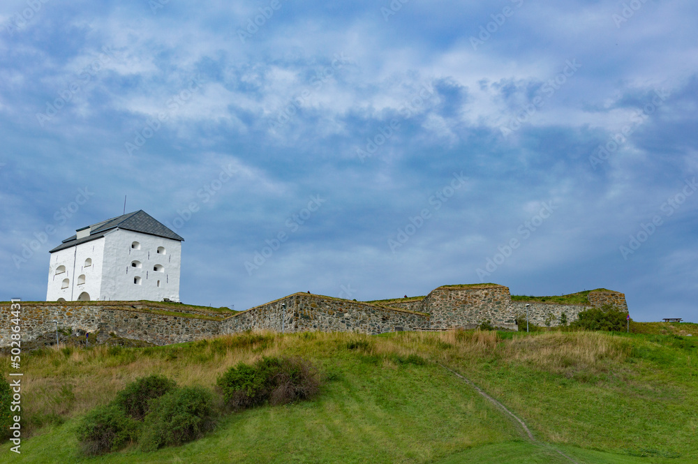 Citadel of the Kristiansten fortress in Trondheim, Norway. White walls with gun ports, green grass, grey cloudy sky