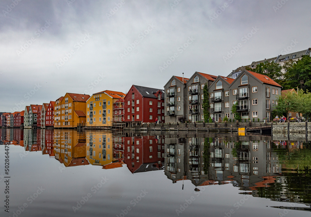 The Nidelva river flowing through the Trondheim city in Norway. Old wooden storehouses on the river bank, grey water, cloudy sky