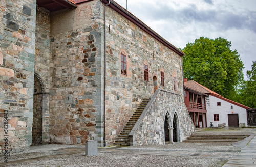 Bishop`s palace in Trondheim, Norway. Blue and grey sky with clouds, grey and brown medieval stone walls, green trees