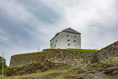 Citadel of the Kristiansten fortress in Trondheim, Norway. White walls with gun ports, green grass, grey cloudy sky
