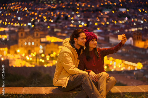 Pareja de turistas sentados en el mirador tomándose un selfie hacia la plaza de Cuzco