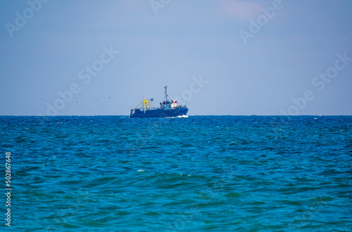 Fishing boat in blue sea and clear sky with birds flying overhead.