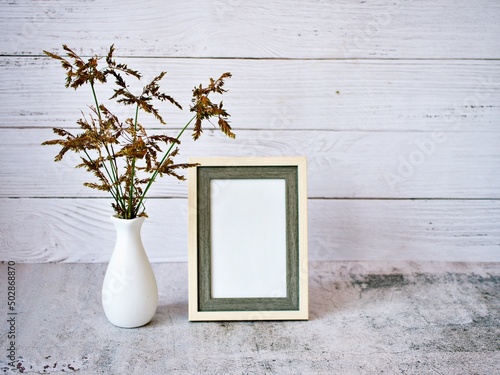 Grass in vase on table and old vintage background Empty photo frame ,Cyperus haspan flowerhead dry grass still life ,copy space for letter ,wooden old wall black and white ,old style ,flowers in vase photo