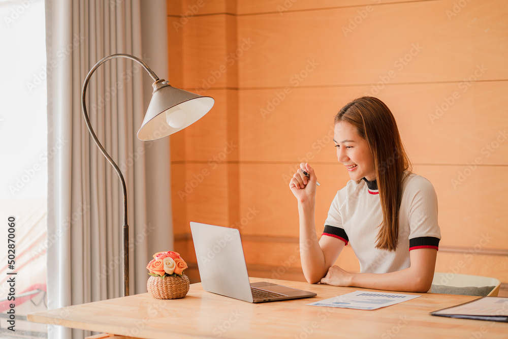 Cropped photo of beautiful Asian female accountant working from home checking documents and using notebooks and calculators. Saving at home smiling happily at work. Cropped photo of beautiful Asian female accountant working from home checking documents and using notebooks and calculators. Saving at home smiling happily at work.