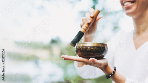 Foto Young smiling woman playing on the brass Tibetan singing bowl outdoor, banner