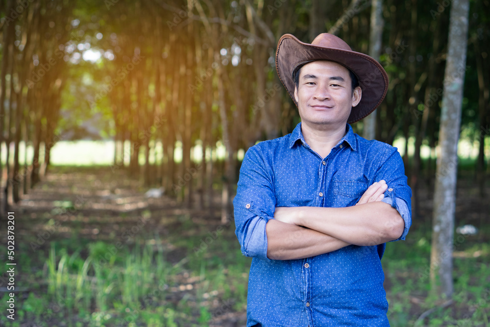 Portrait of handsome Asian man gardener wear hat, blue shirt, crossed arms on chest, feel confident, stand at forest garden. Concept : forester. Forest conservation. Growing  economic trees as garden.
