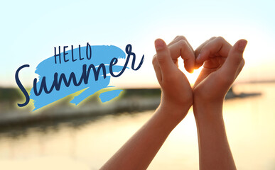 Cute little girl making heart with her hands outdoors at sunset. Hello, summer