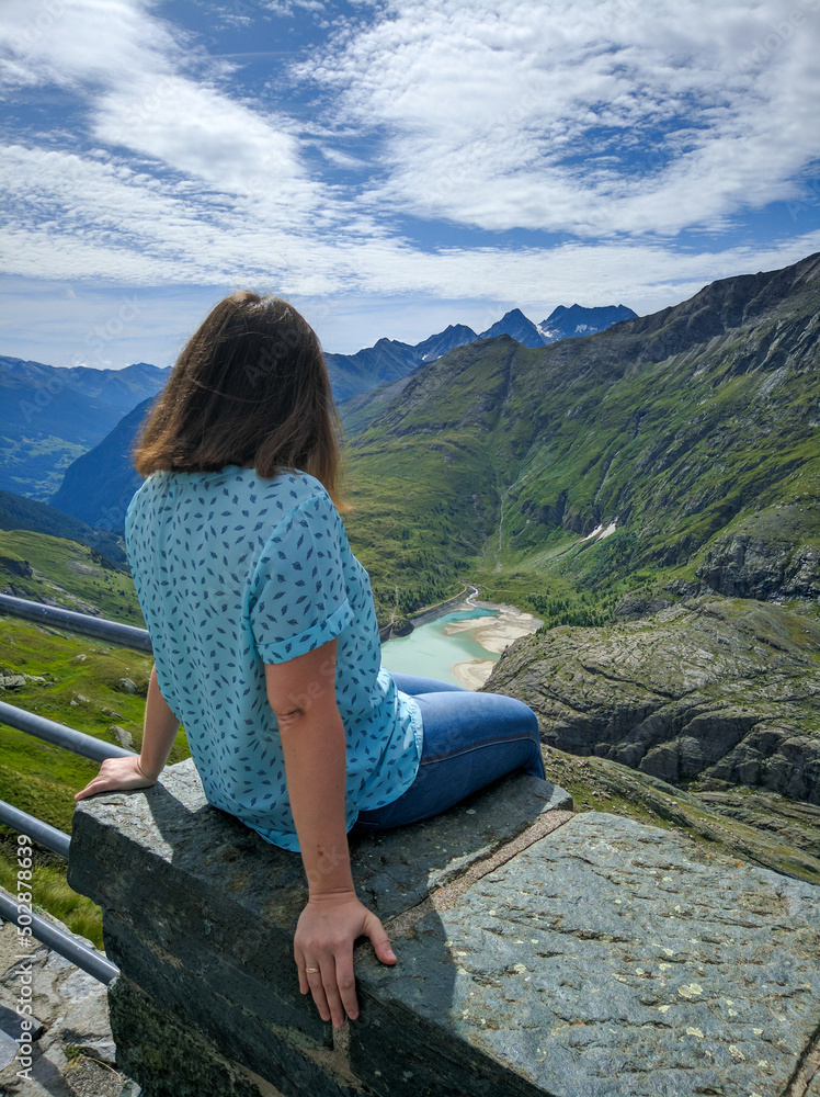 Grossglockner, Austria - August 17, 2019: Alpine road Grossglockner. The girl sits on a stone and admires the beautiful views of the Alps. Vertical