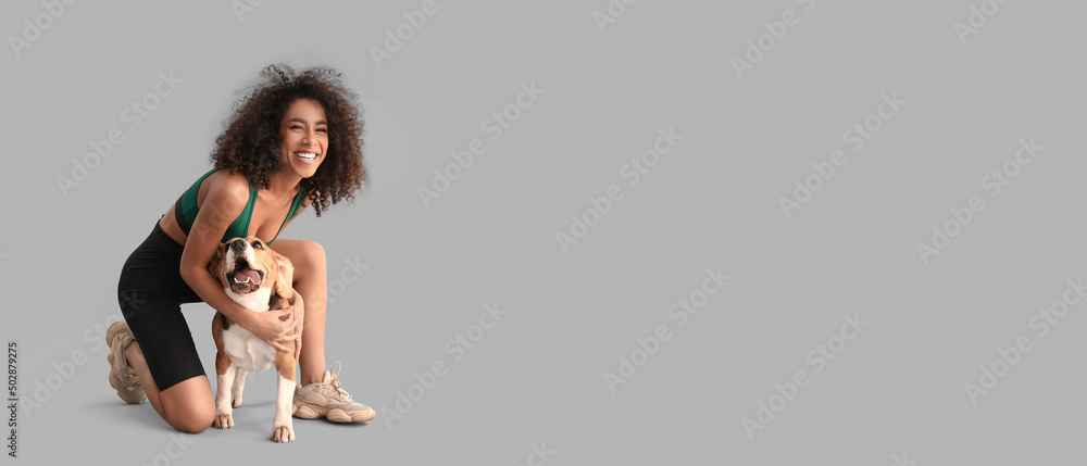 Sporty African-American woman with cute dog on grey background - obrazy, fototapety, plakaty 
