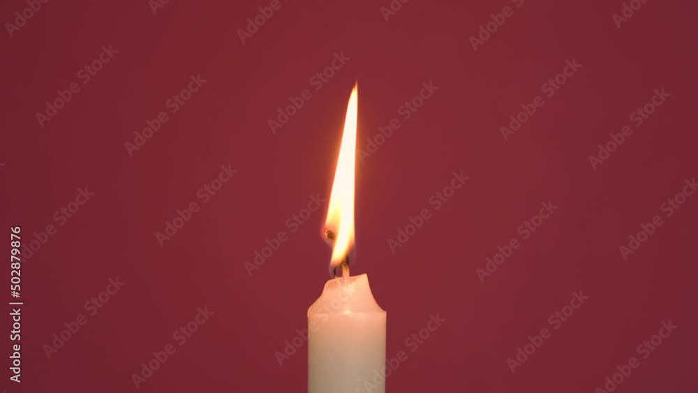 Close-up of a single wax candle burning. Isolated glowing candles on a red background. Background or illustration of a festive ceremony, a celebration, birthday or Christmas. Close-up of a single wax candle burning. Isolated glowing candles on a red background. Background or illustration of a festive ceremony, a celebration, birthday or Christmas.