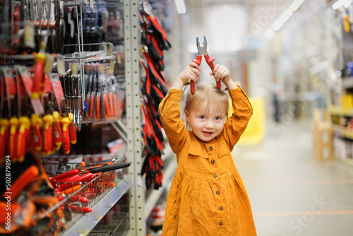 Obraz na plátně Cute girl child in mustard dress in hardware store, child plays with pliers, cho