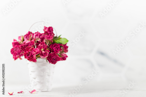 Romance dry pink roses in white basket as bridal bouquet on soft light white table and elegant marble wall  copy space. Elegant floral background for wedding  anniversary  greeting card.