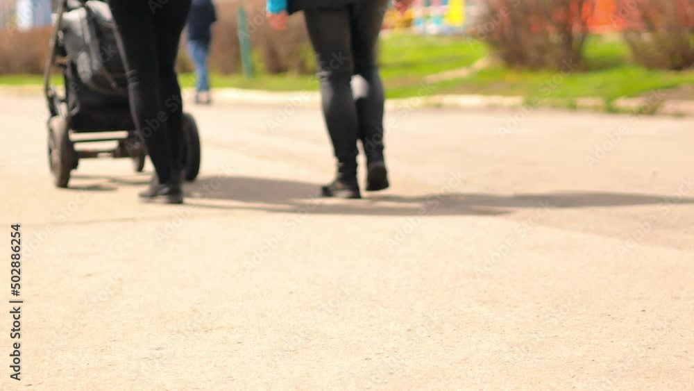 Walking legs of young modern parents with a baby stroller, mom in leather pants, dad in trousers. Walking legs of young modern parents with a baby stroller, mom in leather pants, dad in trousers.