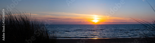 Panoramic landscape background banner panorama of sunset or sunrise and grass of the dune on the North Sea photo