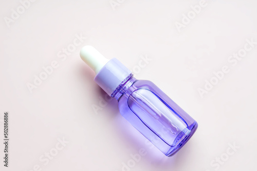purple dropper bottle with essential oil or face serum on beige background. Daily routine treatment for young skin