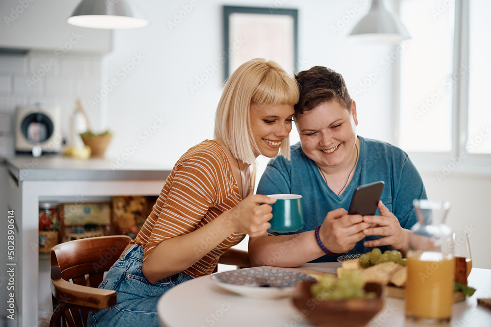Happy lesbian couple using smart phone while having breakfast at dining table.