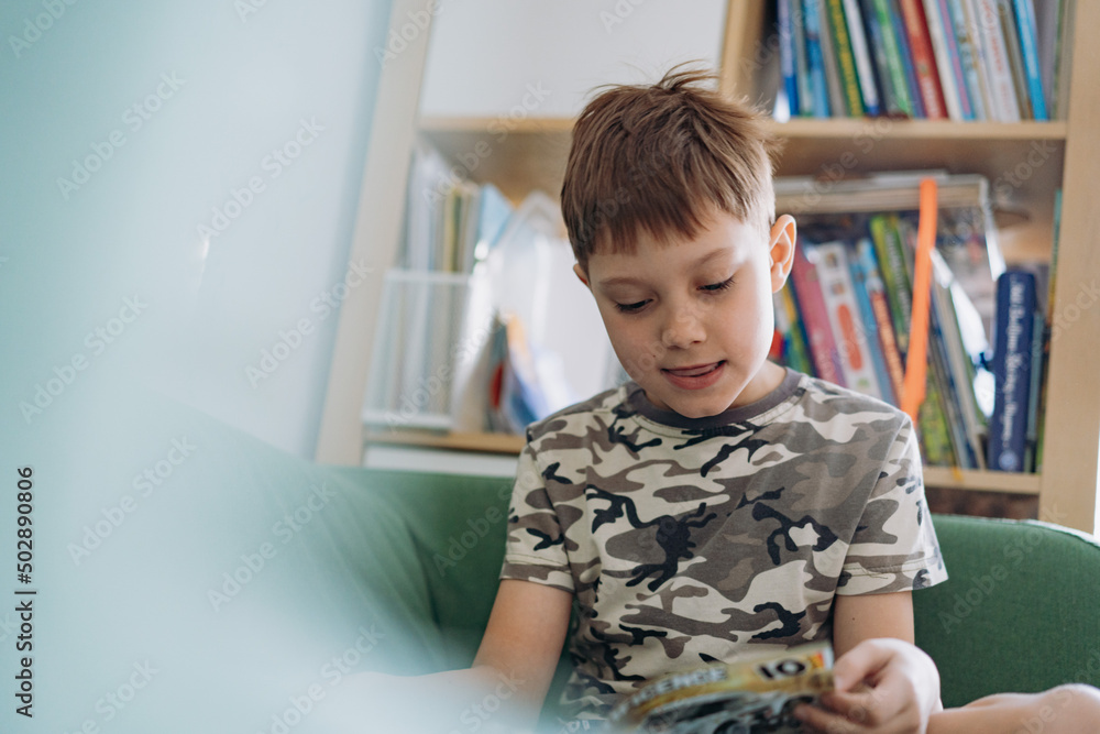 Little caucasian boy reading a book sitting on couch Little caucasian boy reading a book sitting on couch