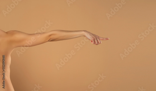 Young woman's stretched arm and touching imaginary product with index finger. Isolated on beige background