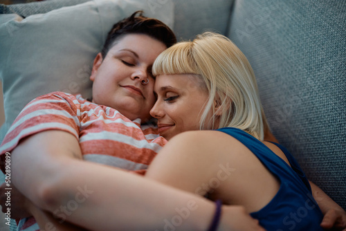 Loving female couple napping embraced on sofa at home.