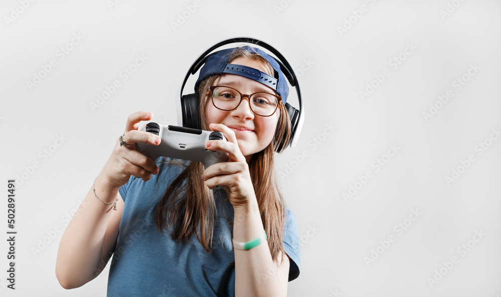 Teen girl in headphones plays video games with a gamepad in her hands. Gamer girl. Teen girl in headphones plays video games with a gamepad in her hands. Gamer girl.