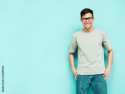Portrait of handsome smiling stylish hipster lambersexual model.Man dressed in T-shirt and jeans. Fashion male isolated in studio. Posing near blue wall. Cheerful and happy © halayalex