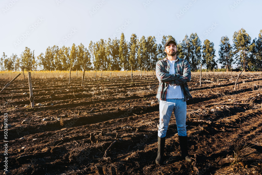 Young latin farmer man with crossed arms in the middle of the farmland. Agricultural sustainability concept.