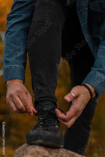 Stylish man in fashionable clothes and black sneakers laces up and walks in an autumn park