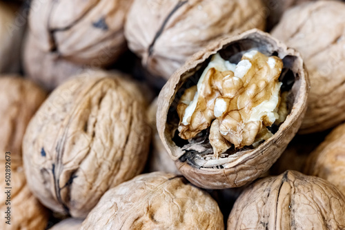 Closeup of split raw walnut on pile of whole walnuts with shells