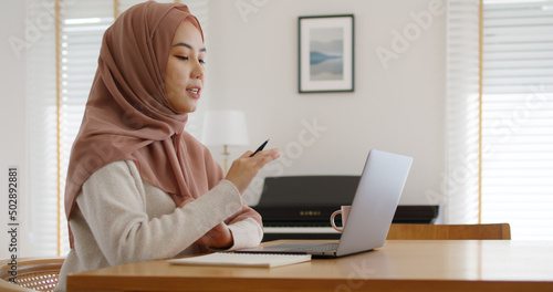Asia arab people young woman wear hijab headscarf plan study MBA college class note idea data in sale report remote work at home on laptop. Happy advisor lifestyle smile cowork smart workforce job.
