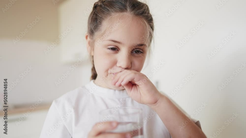 child girl drinking water from a glass cup. the problem of lack of clean drinking water in the world lifestyle. little girl in the kitchen drinks drinking water from a transparent glass cup