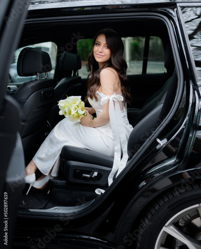 Beautiful bride with black hair in a white narrowed dress gets out of the car