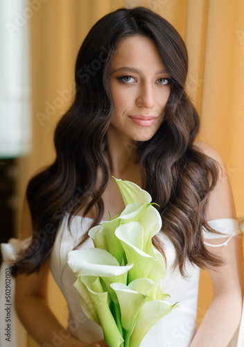 Beautiful young bride posing with a bouquet in her hands by the window. High quality photo