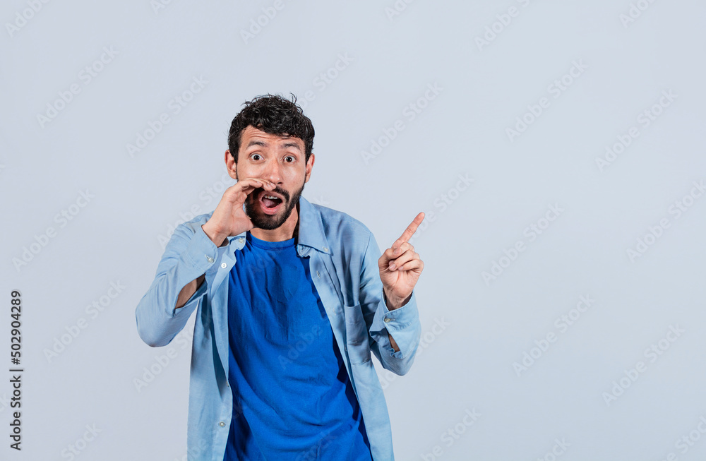 Fototapeta premium Handsome man whispering and pointing to the side, guy whispering and pointing fingers to the side, latin guy pointing at blank space