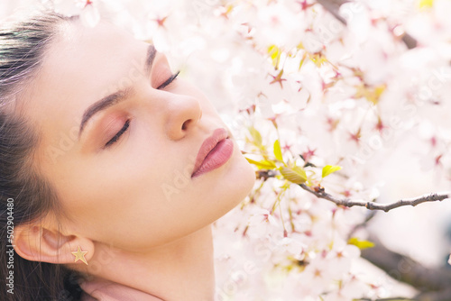 Beauty  lifestyle and nature concept. Beautiful brunette woman portrait in white sakura blossom background during spring time in sunny day. Model with day make-up and closed eyes dreaming