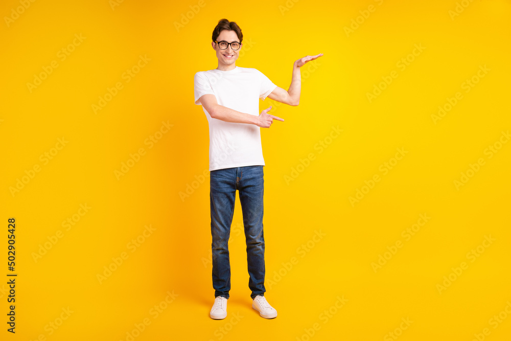 Full size photo of young cheerful guy indciate finger empty space measure size advertise isolated over yellow color background Full size photo of young cheerful guy indciate finger empty space measure size advertise isolated over yellow color background