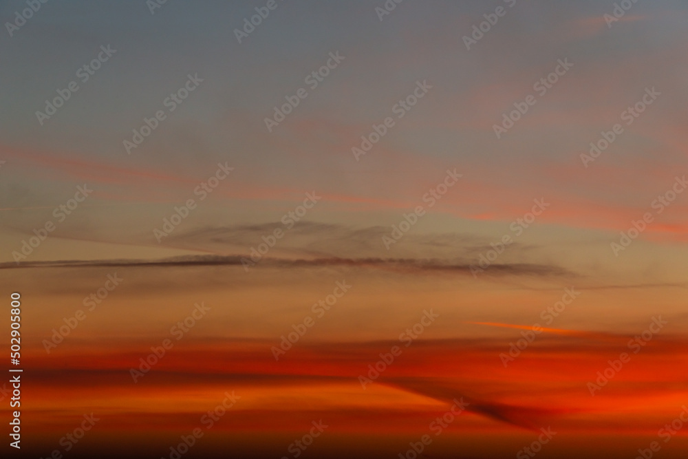 Panoramic view with gradient deep orange sky, illuminated clouds at bloody sunset as a background.