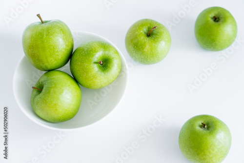 top view of green and juicy apples in bowl on white.